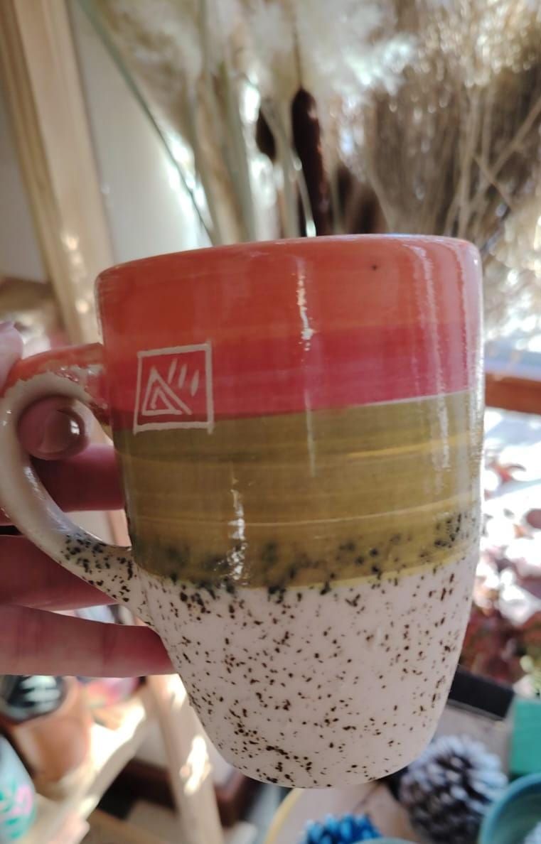 Taza de cerámica con esmaltado turquesa y azul marino sobre blanco moteado, colocada sobre un paño blanco.