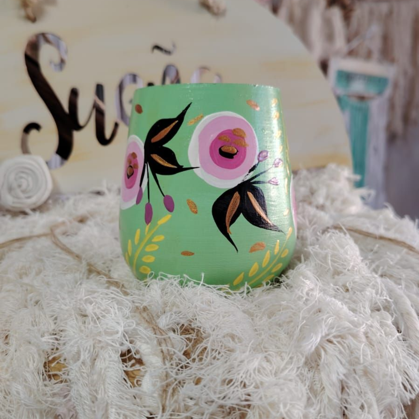 Vidrio pintado de verde con flores rosas, sobre una superficie blanca esponjosa.