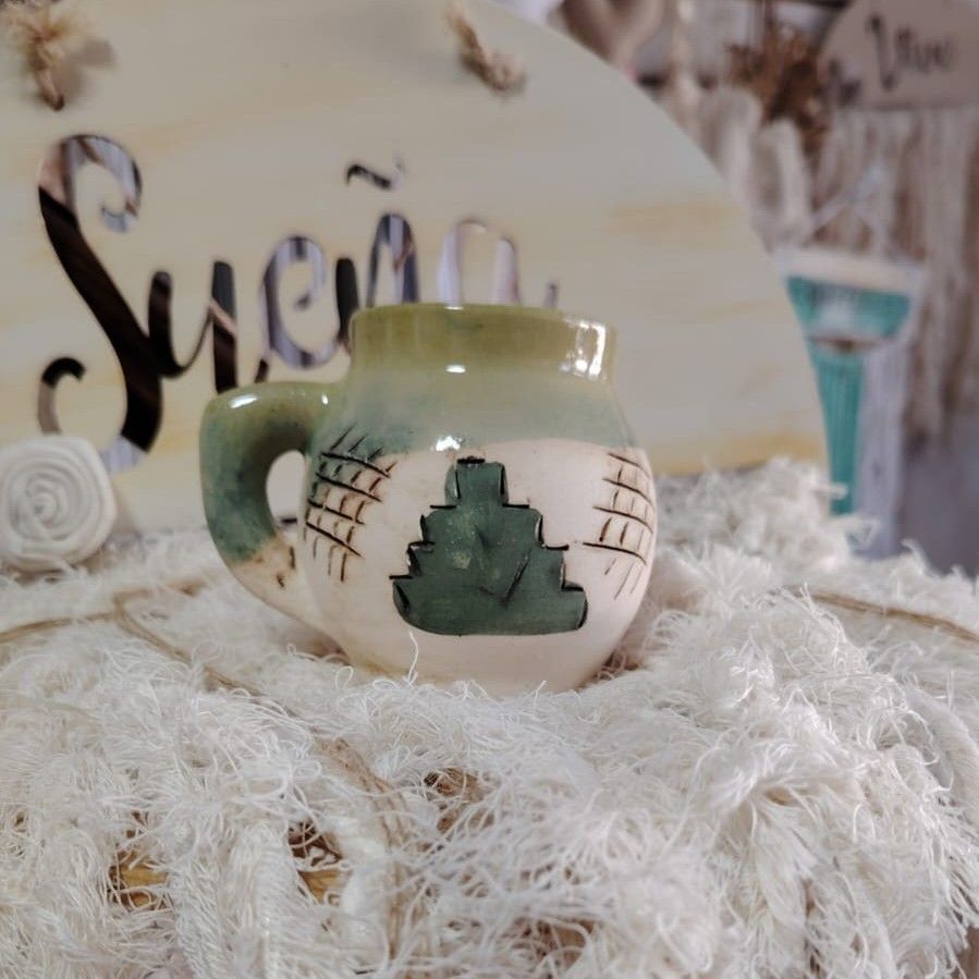 Taza de cerámica con colores verde, blanco y marrón, sobre una superficie blanca esponjosa.