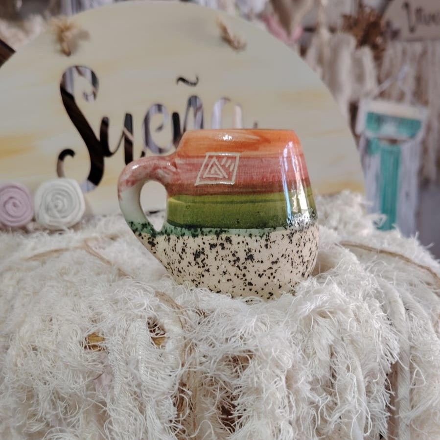Taza de cerámica colorida sobre tela blanca texturizada, letrero "Sueño" de fondo.