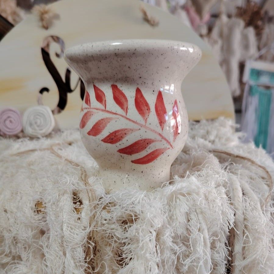 Jarrón de cerámica con un pájaro pintado en tonos naranja, rojo y azul sobre una base blanca y esponjosa.