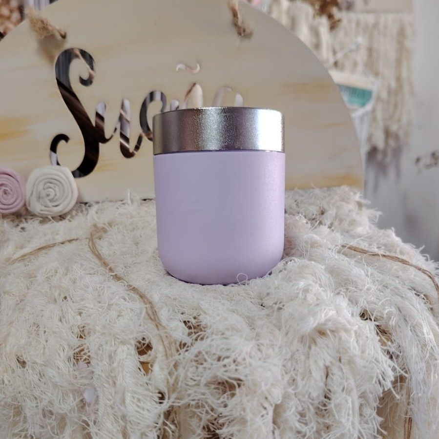 Un vaso de color lila con borde plateado reposa sobre una manta blanca y esponjosa.