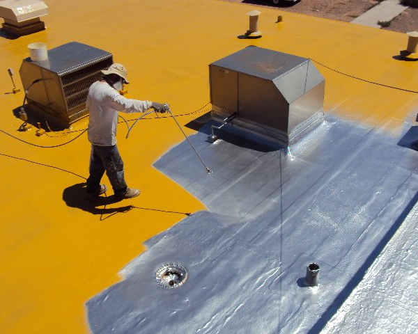 Person applying silver sealant to a flat yellow commercial roof.