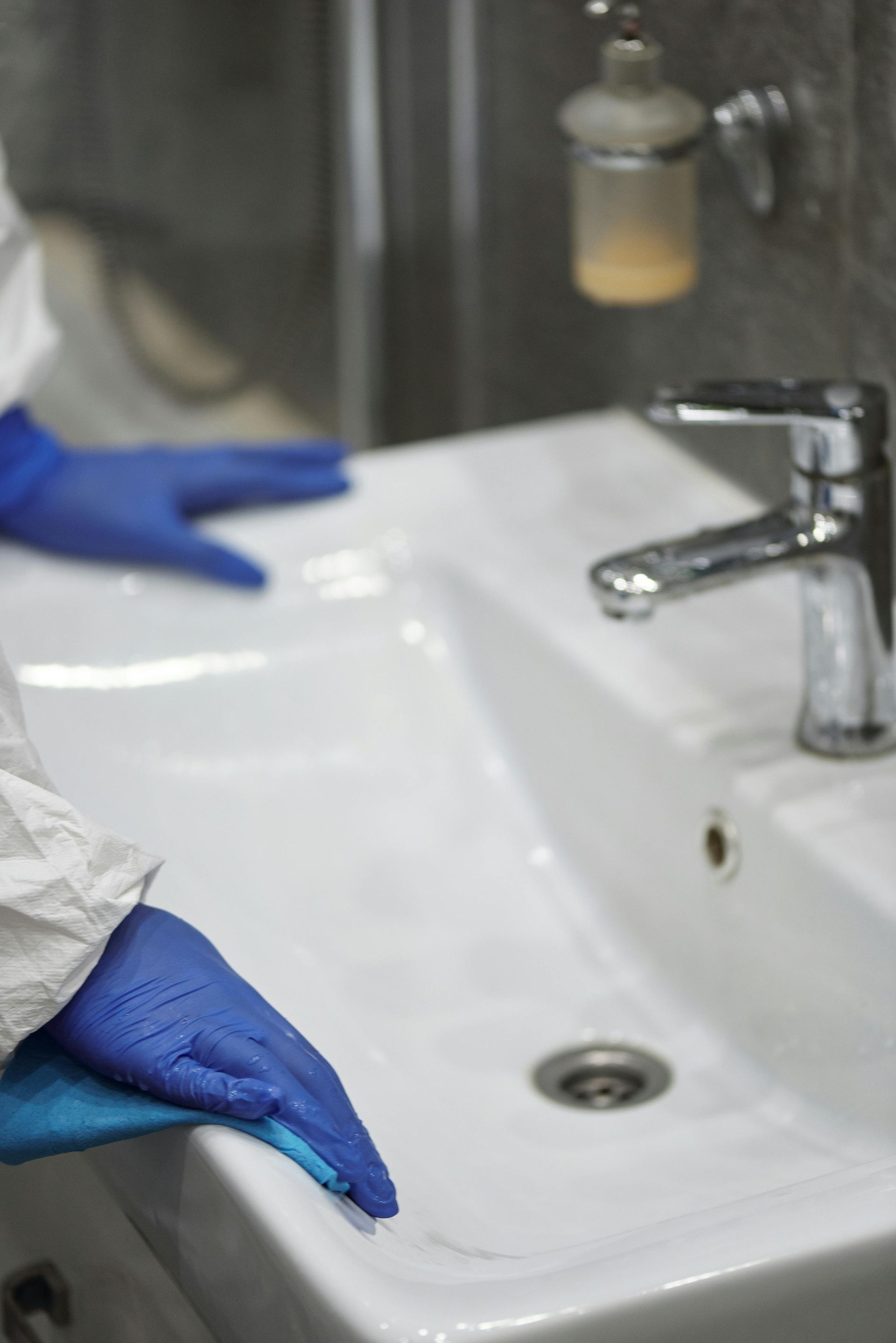 A person wearing blue gloves is cleaning a bathroom sink.