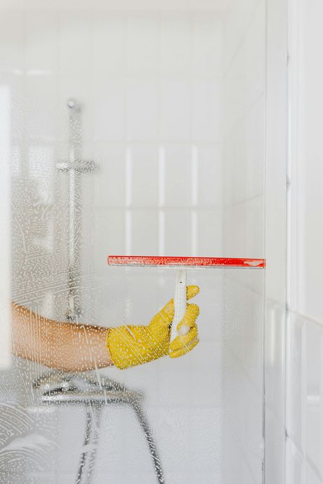 A person is cleaning a shower door with a squeegee.