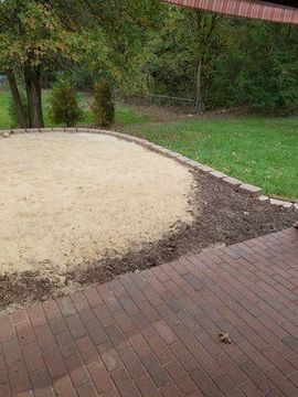 A brick patio with a sandbox in the middle of it.