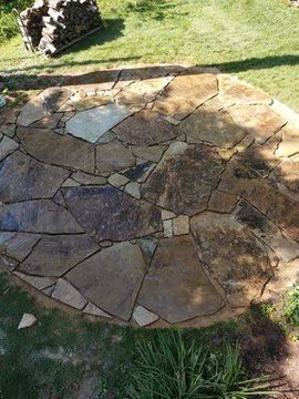 A stone patio in the middle of a lush green field.