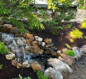 A waterfall is surrounded by rocks and trees in a garden.