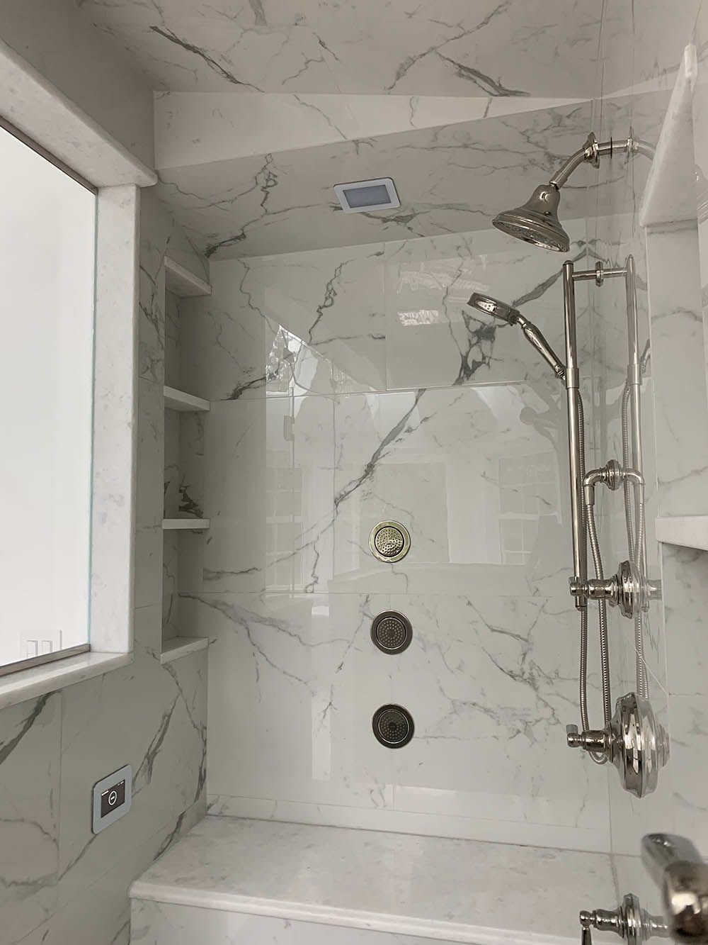 A bathroom with marble walls , a tub , a shower and a window.