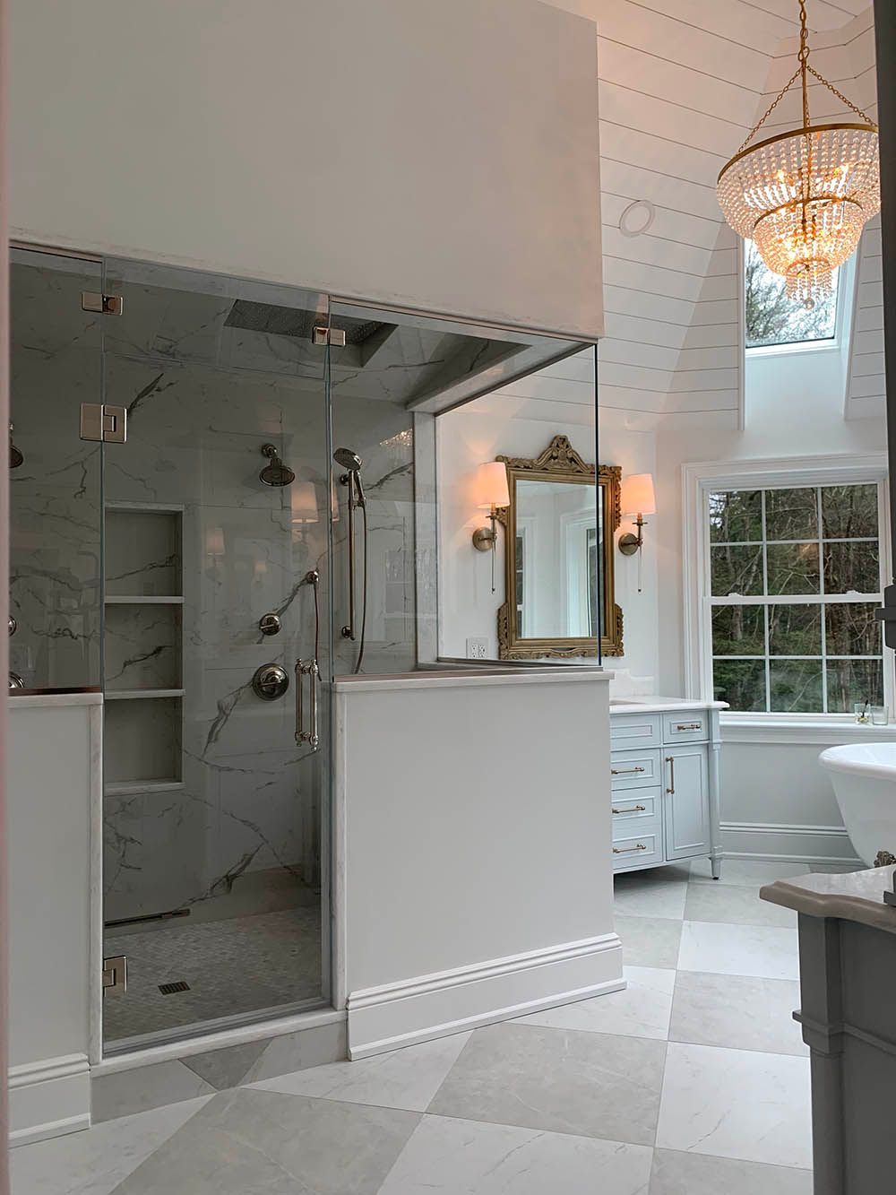 A bathroom with a walk in shower , sink , mirror and chandelier.