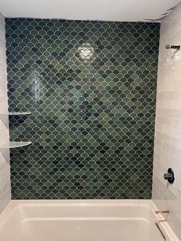 A bathroom with a green tile wall and a bathtub.