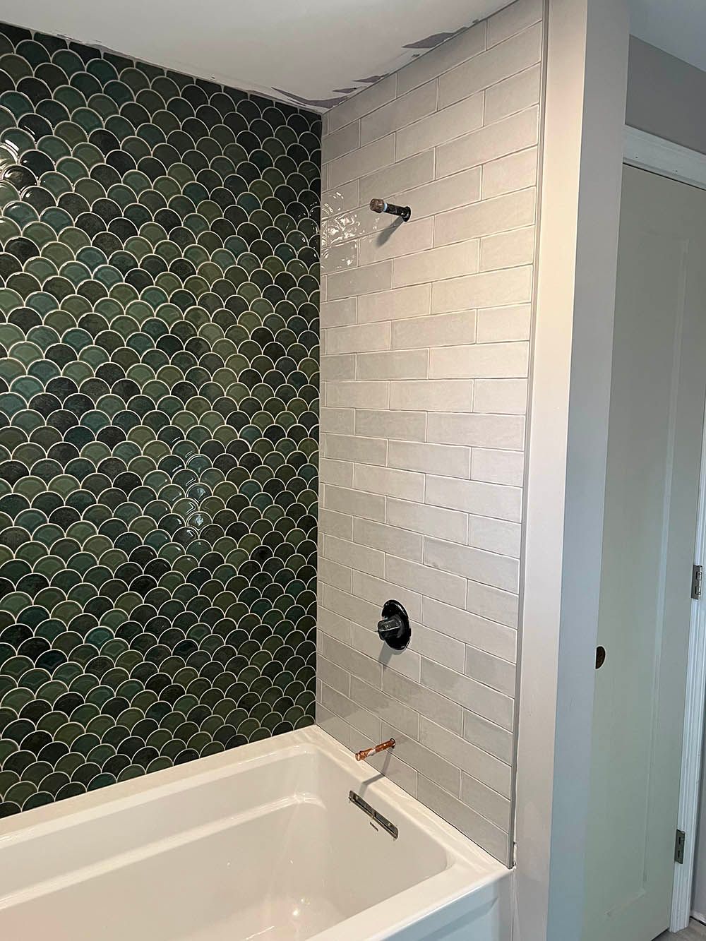 A bathroom with a bathtub , shower , and green tile wall.