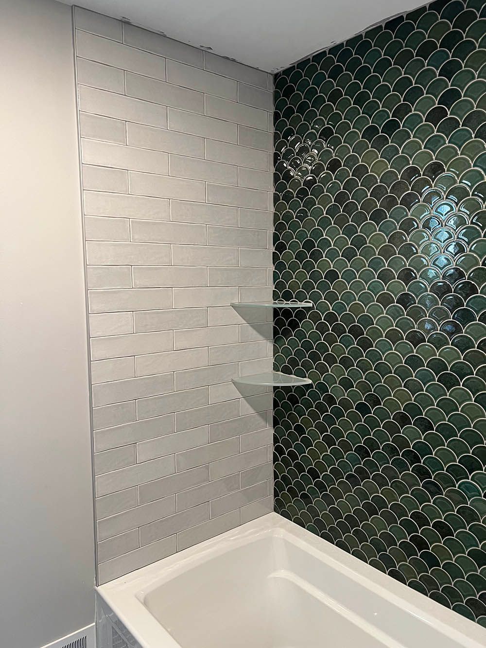 There is a bathtub in the bathroom with a green tile wall.
