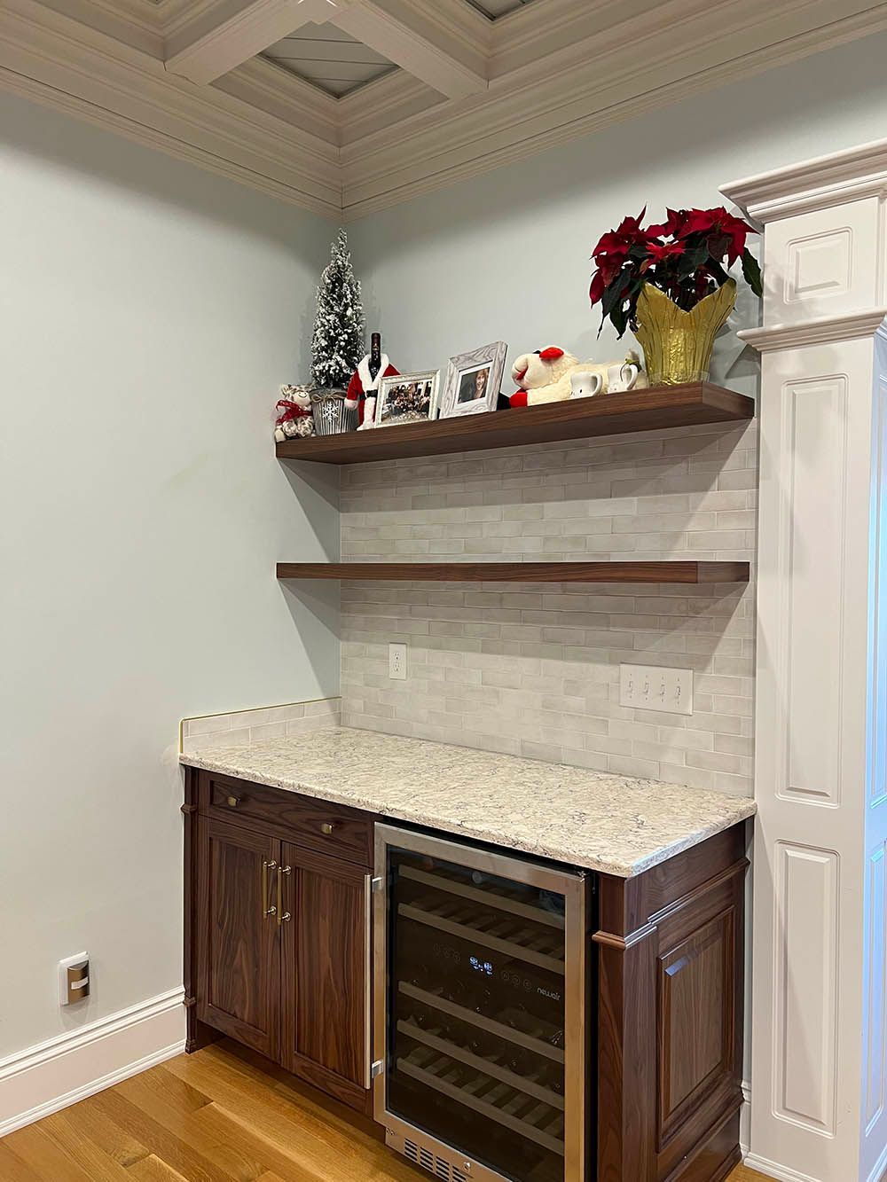 A kitchen with a wine cooler and a shelf above it.