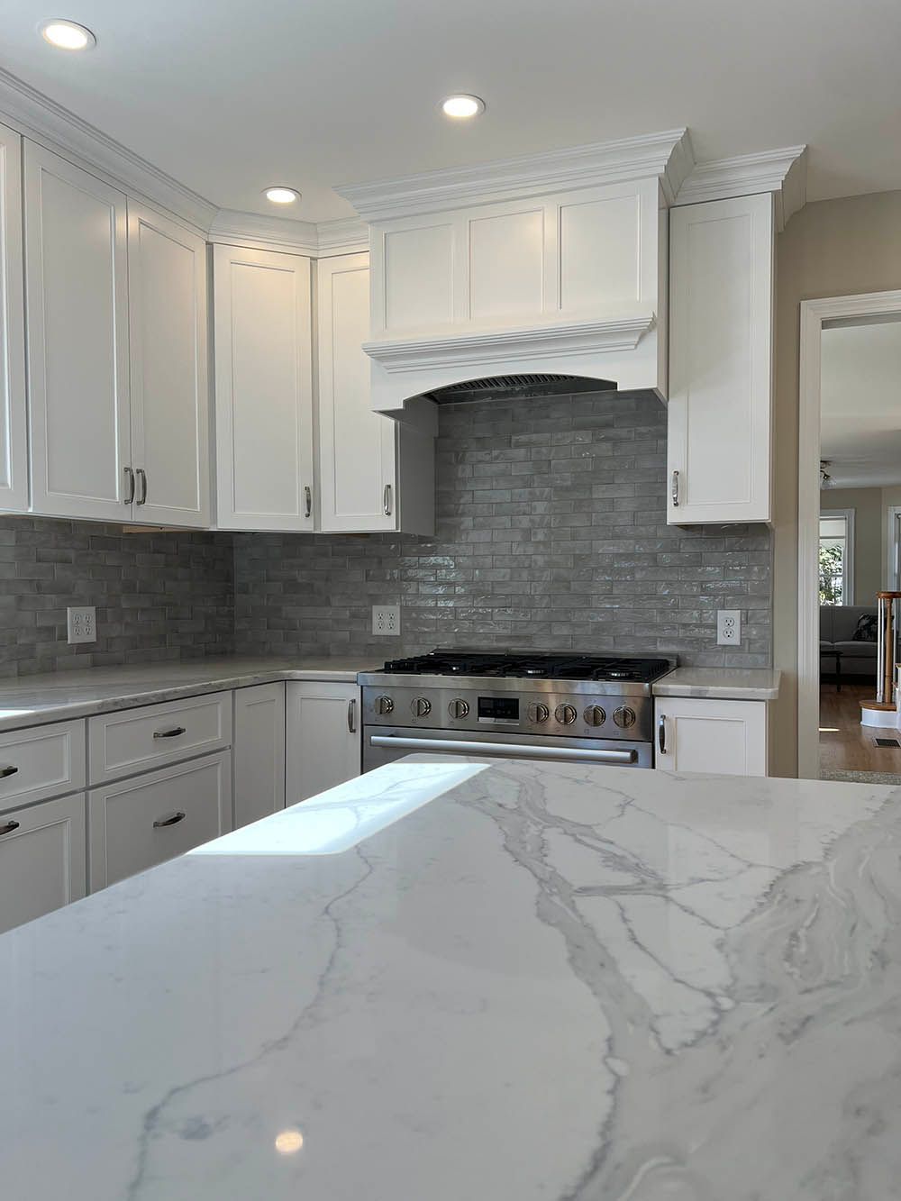 A kitchen with white cabinets , a stove , and a marble counter top.
