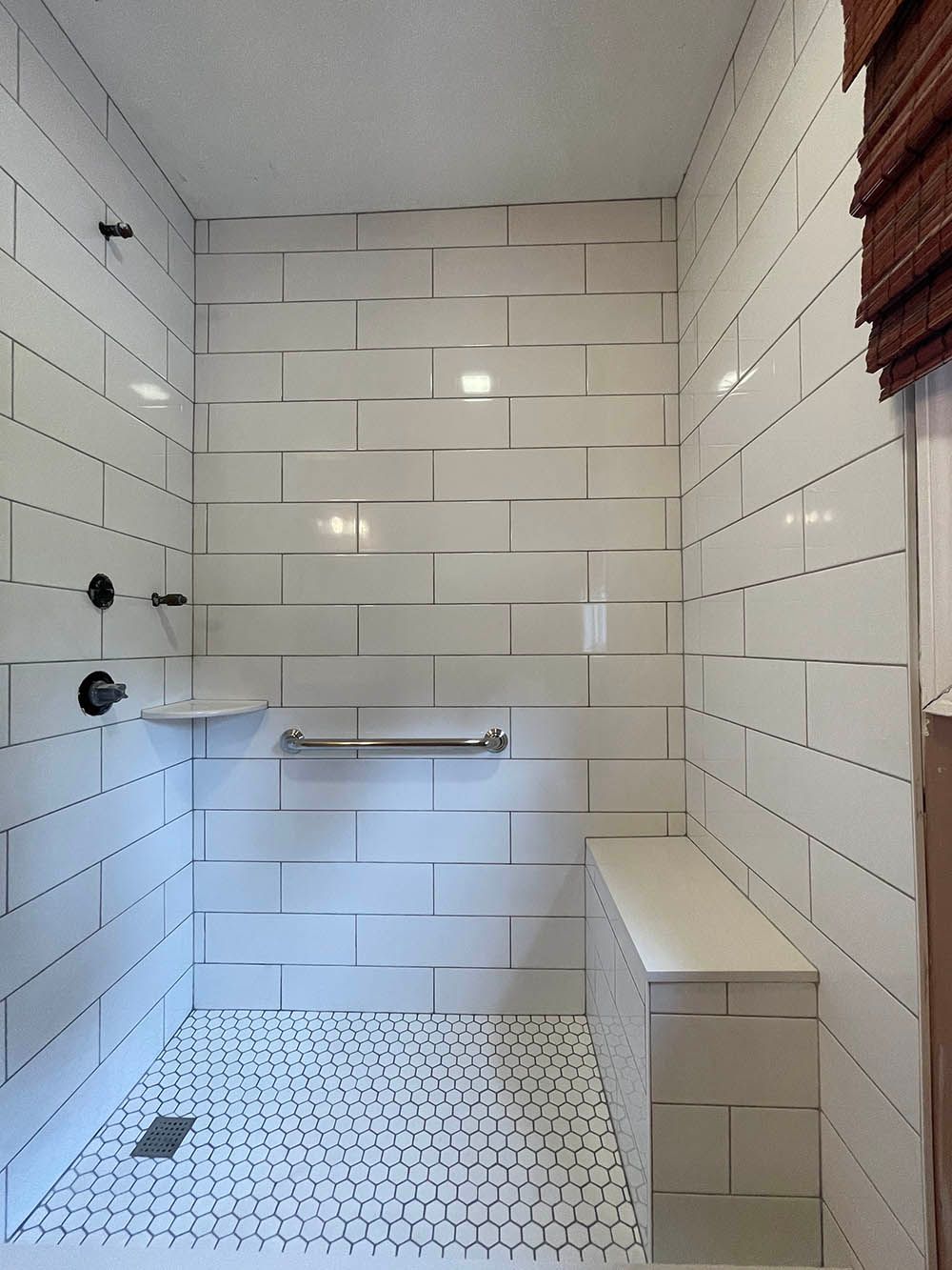 A bathroom with white tiles and a bench in the shower.