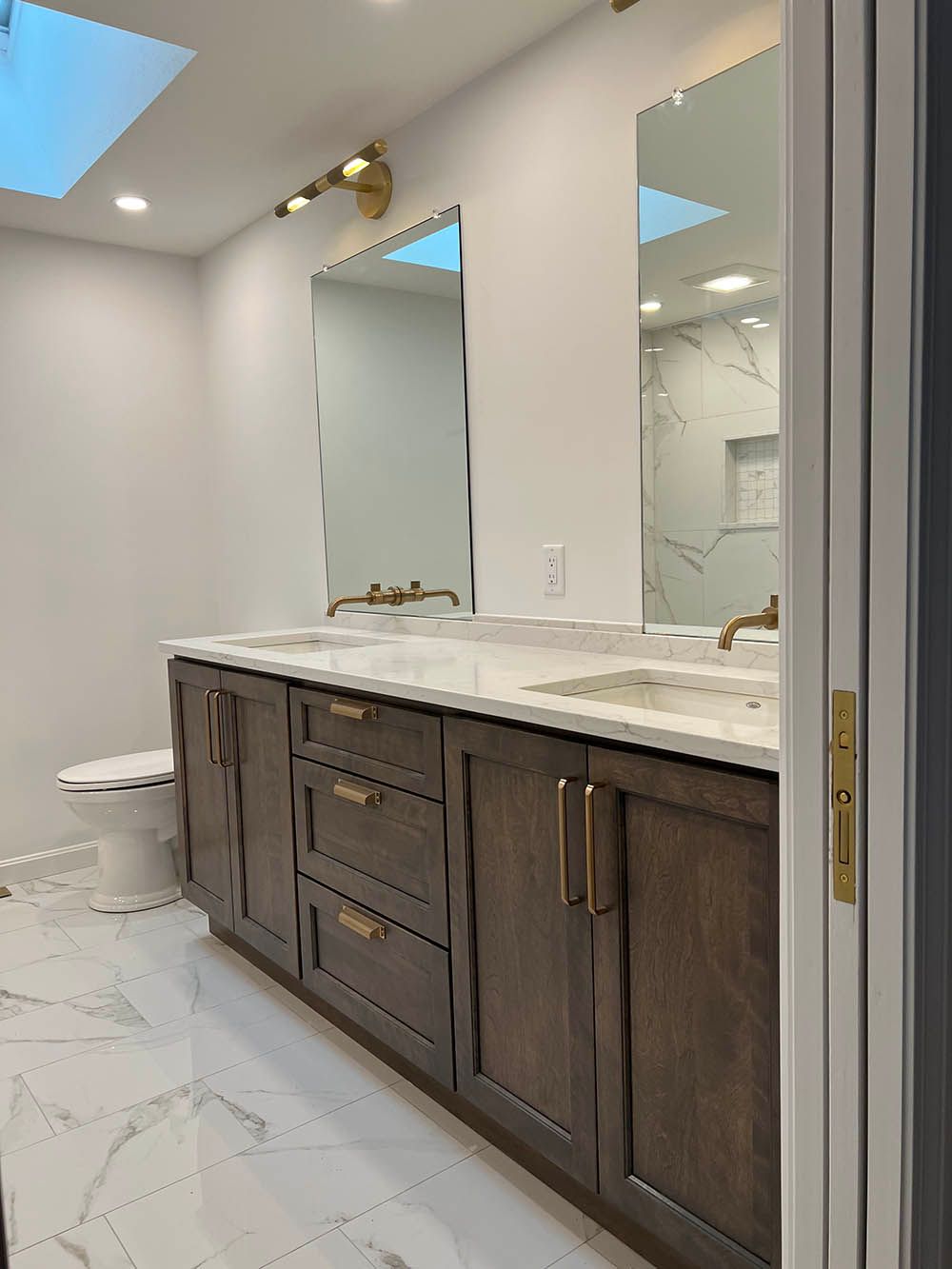 A bathroom with two sinks , a toilet and a skylight.