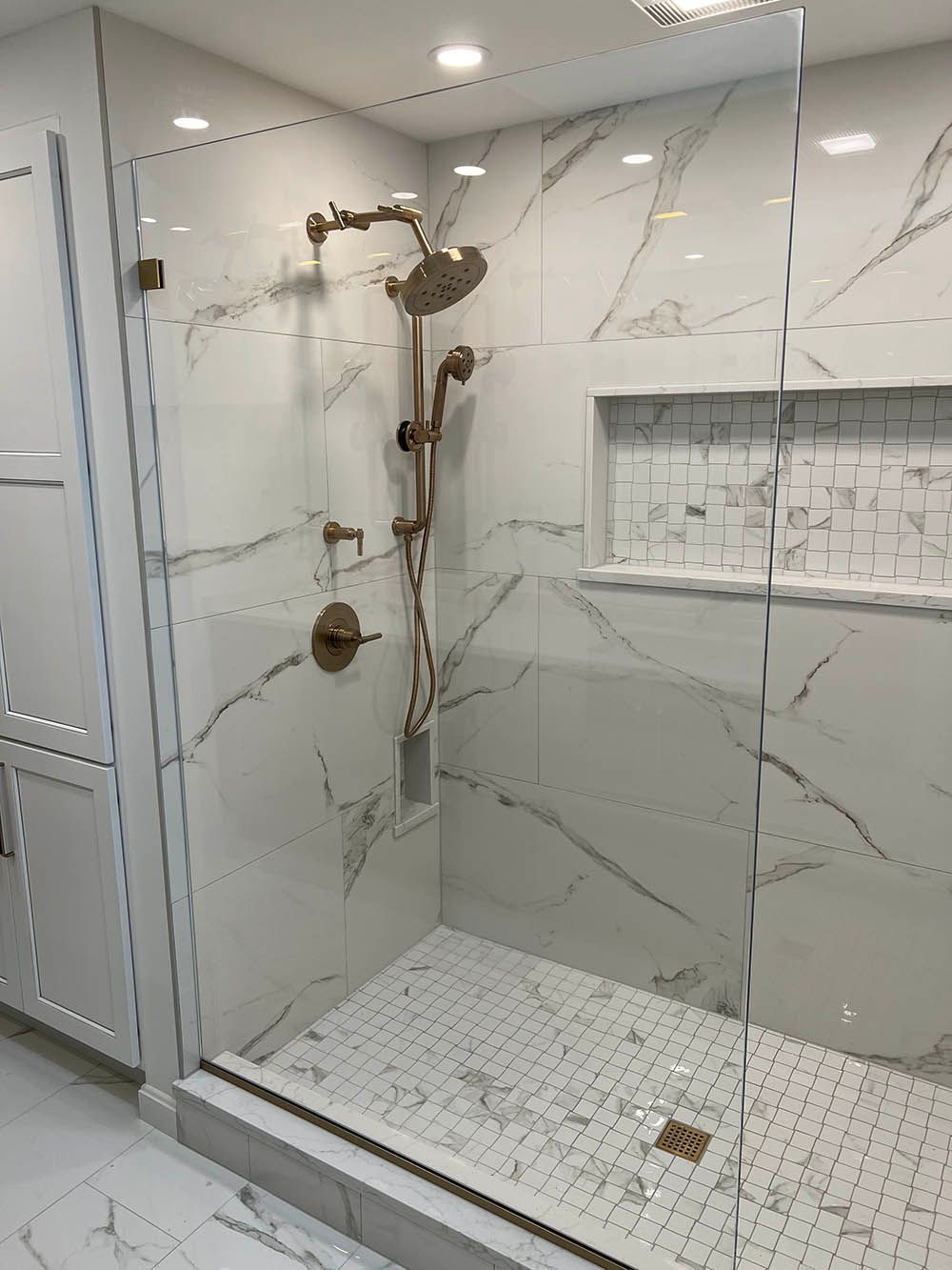 A bathroom with marble tiles and a walk in shower with a glass door.