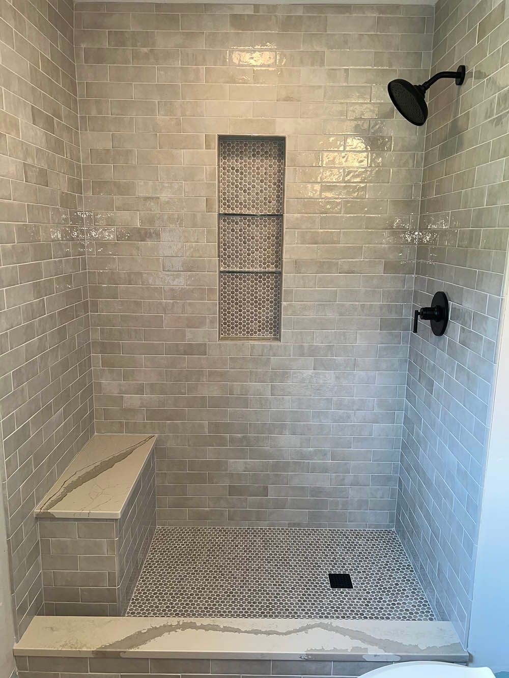 A walk in shower with a bench and a shower head.