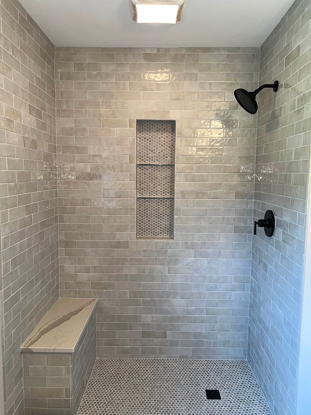 A walk in shower with a bench and a shower head.