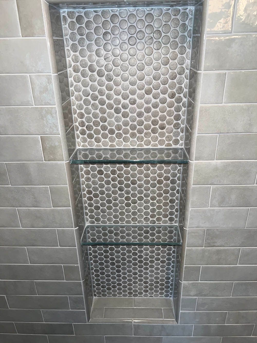 A shower niche with glass shelves in a bathroom.