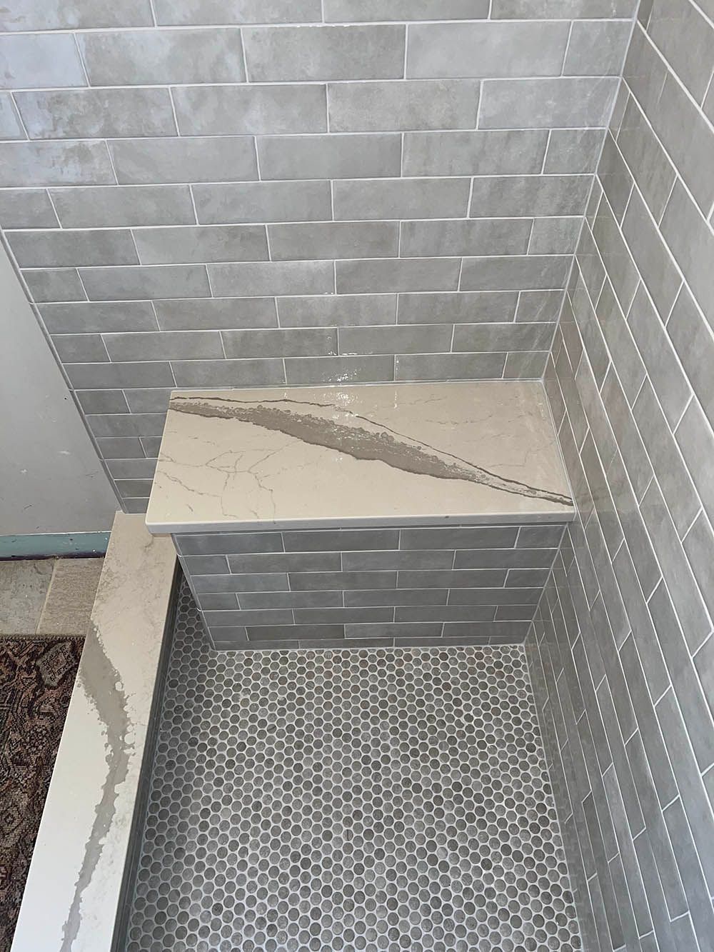 There is a bench in the shower with a marble counter top.