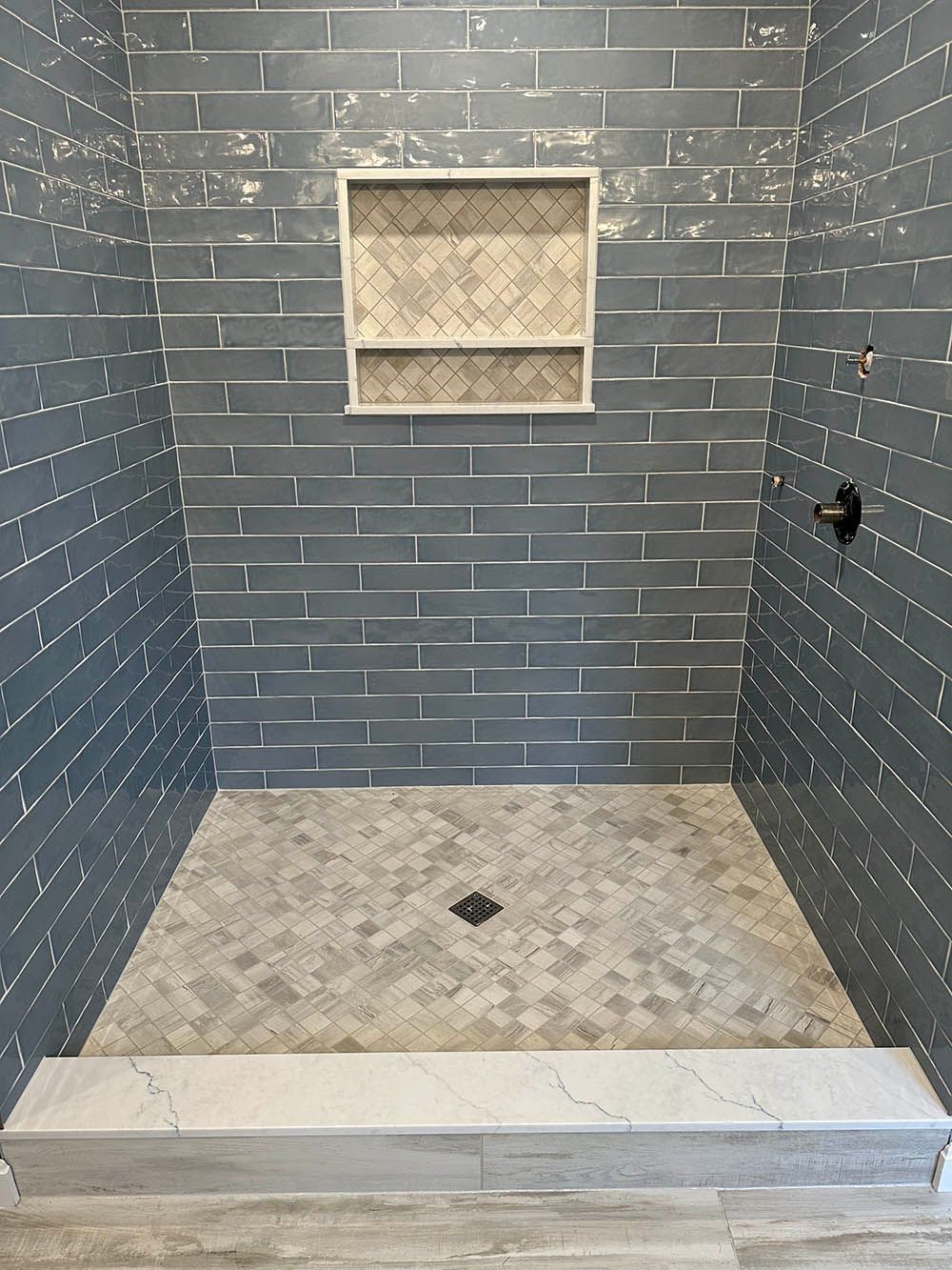 A shower stall with a brick wall and a tiled floor.