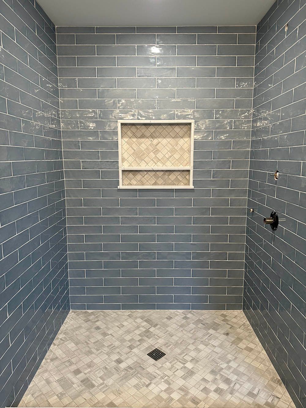 A shower with a brick wall and a tiled floor.