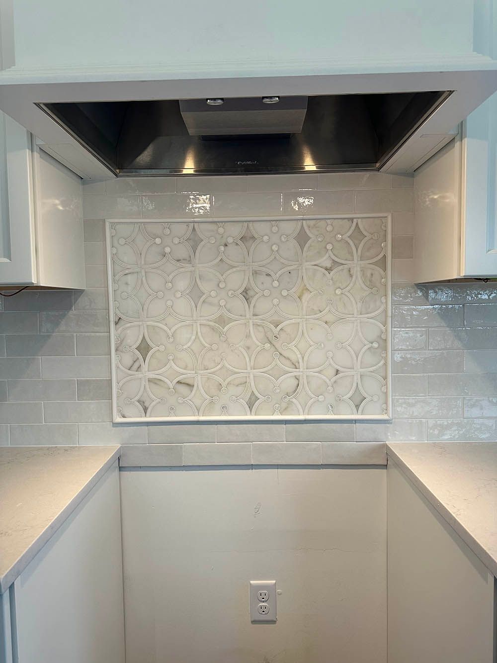 A kitchen with white cabinets and a stainless steel hood.