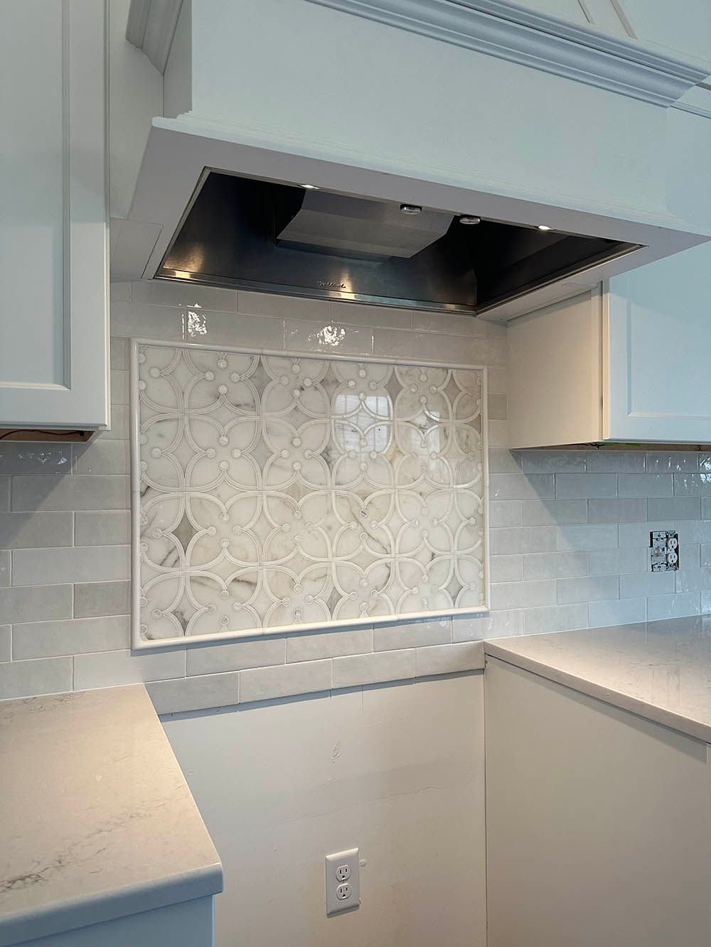 A kitchen with white cabinets and a hood above the counter.