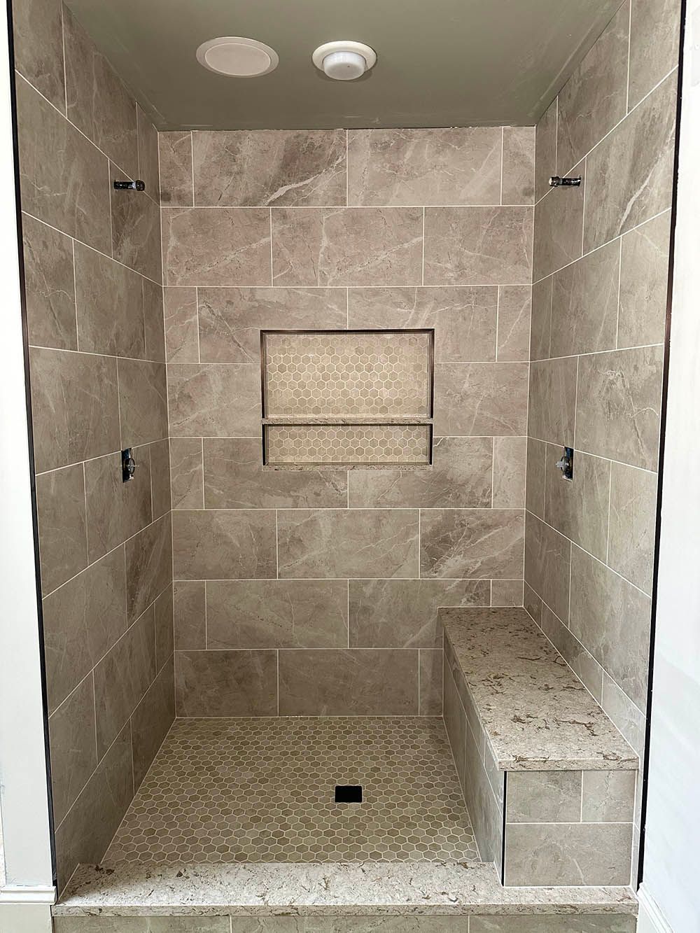 A walk in shower with a bench and a shelf in the wall.