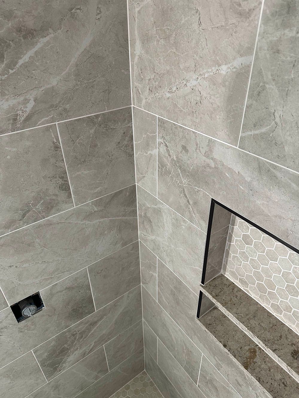 A bathroom with gray tiles and a shelf in the corner.