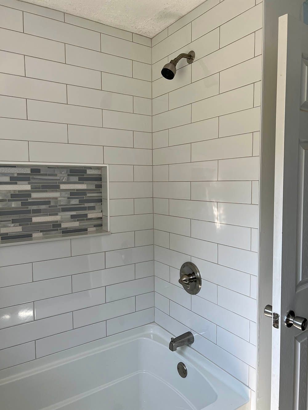 A bathroom with white tiles and a bathtub and shower.