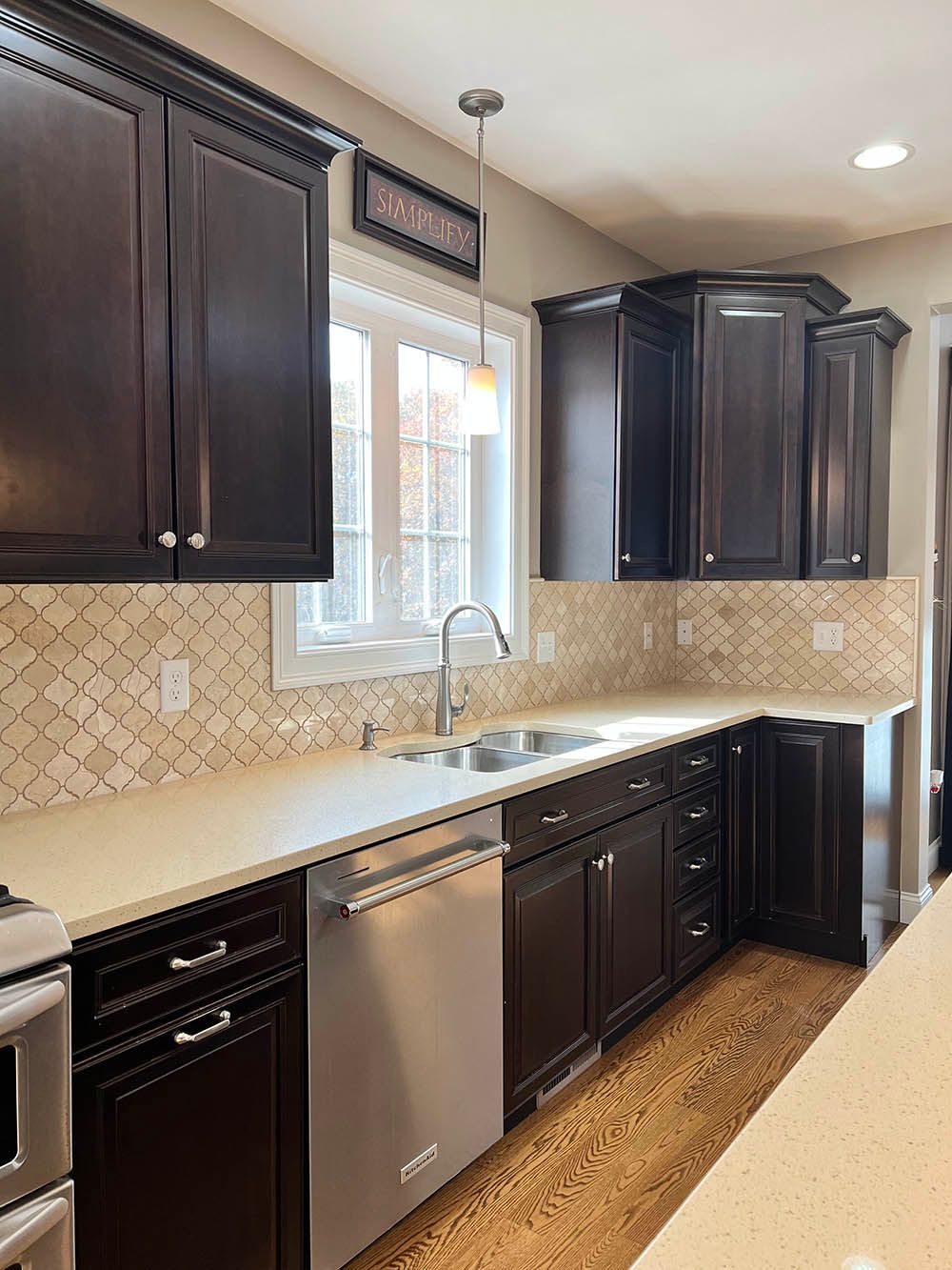 A kitchen with black cabinets , stainless steel appliances , a sink , and a window.