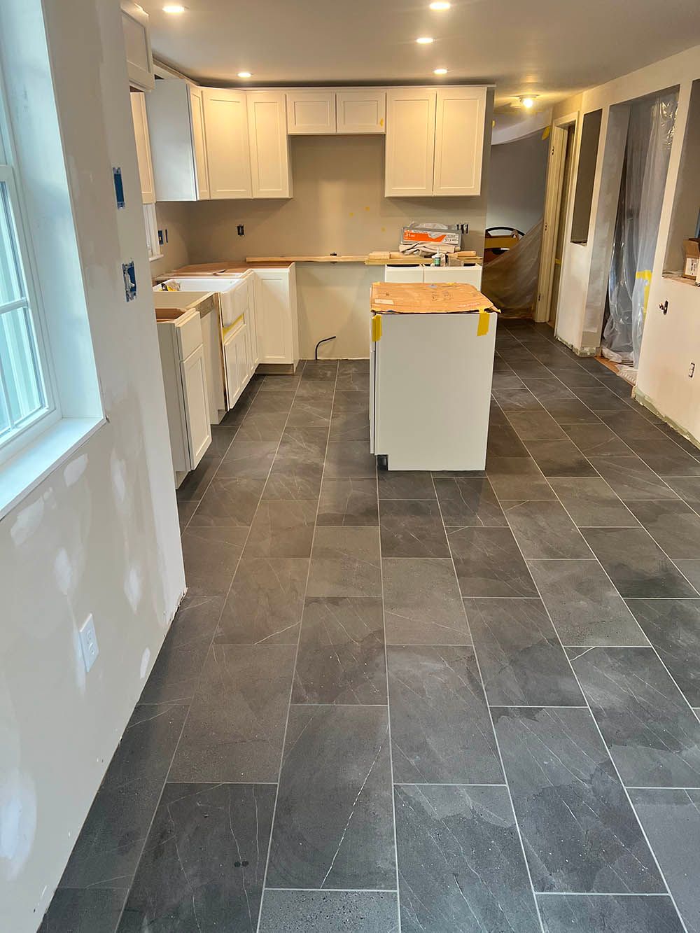 A kitchen under construction with a black tile floor and white cabinets.