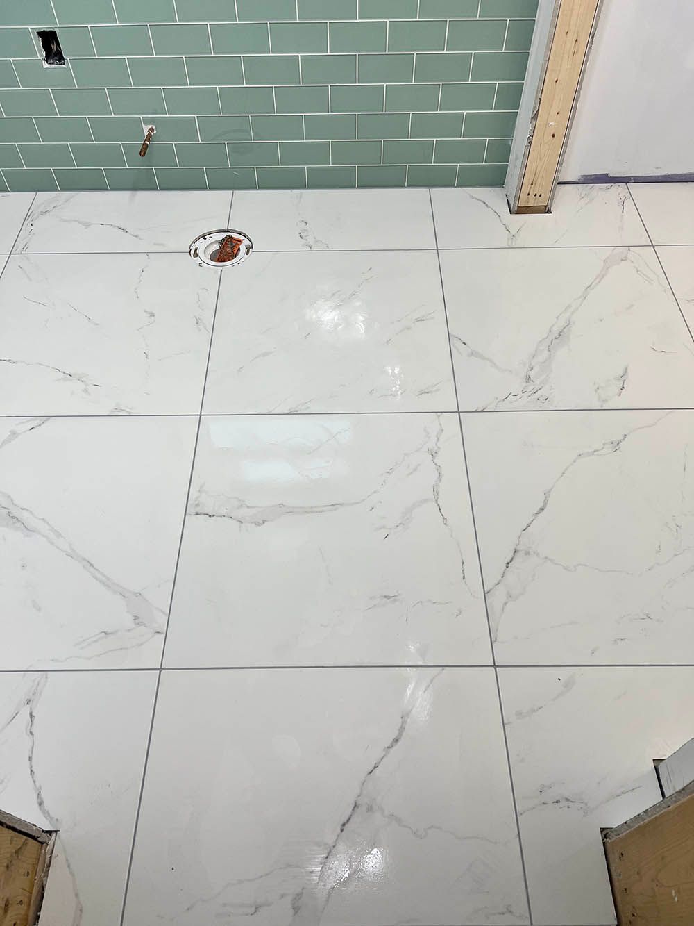 A bathroom floor with white tiles and green subway tiles.