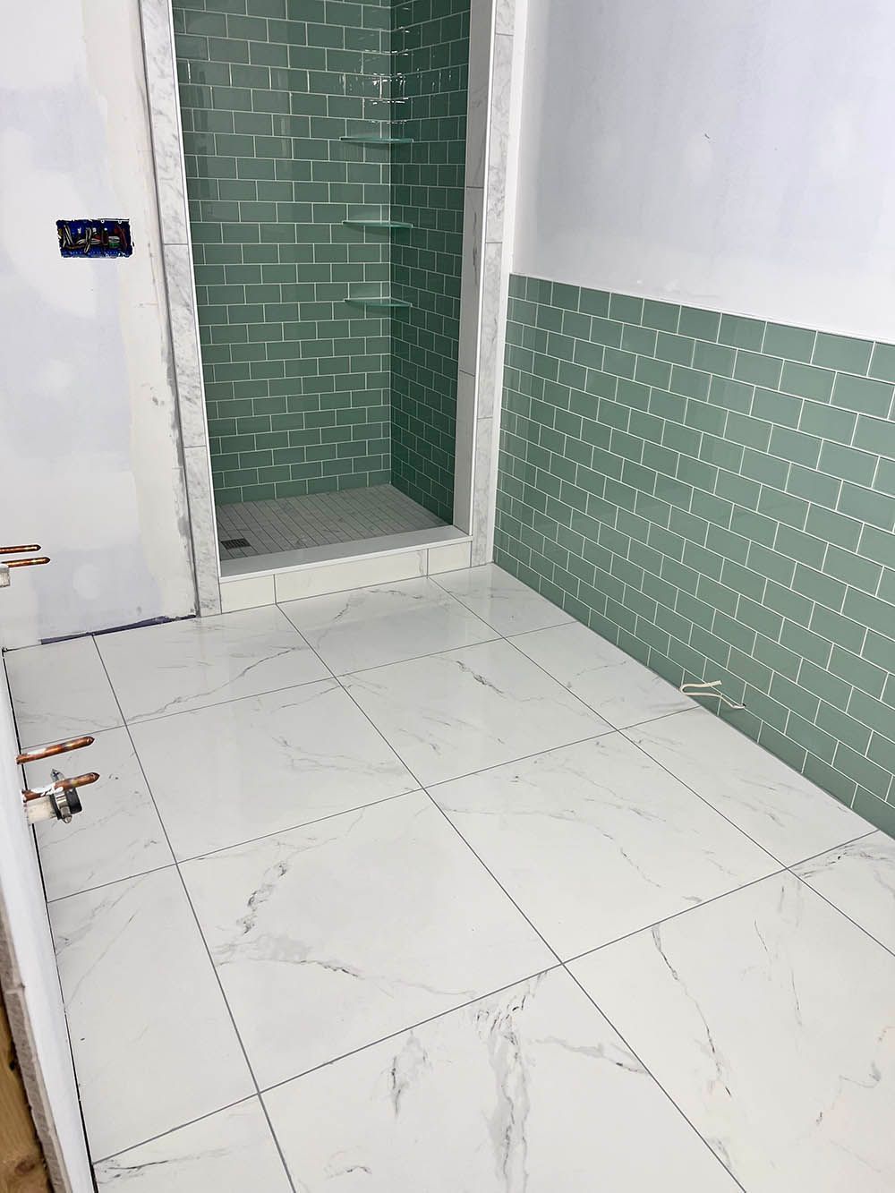 A bathroom with green tiles and white tiles and a walk in shower.