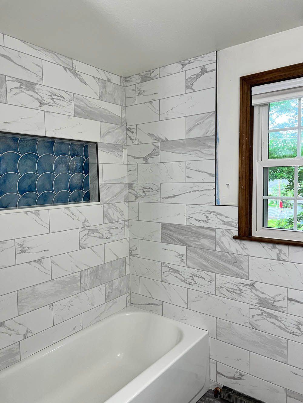 A bathroom with marble tiles , a tub and a window.