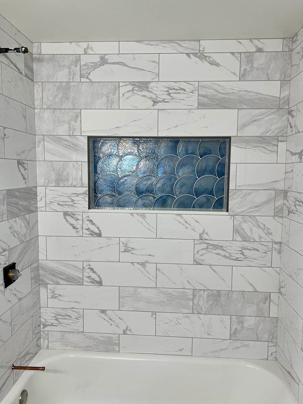 A bathroom with marble tiles and a bathtub with a window in the shower.