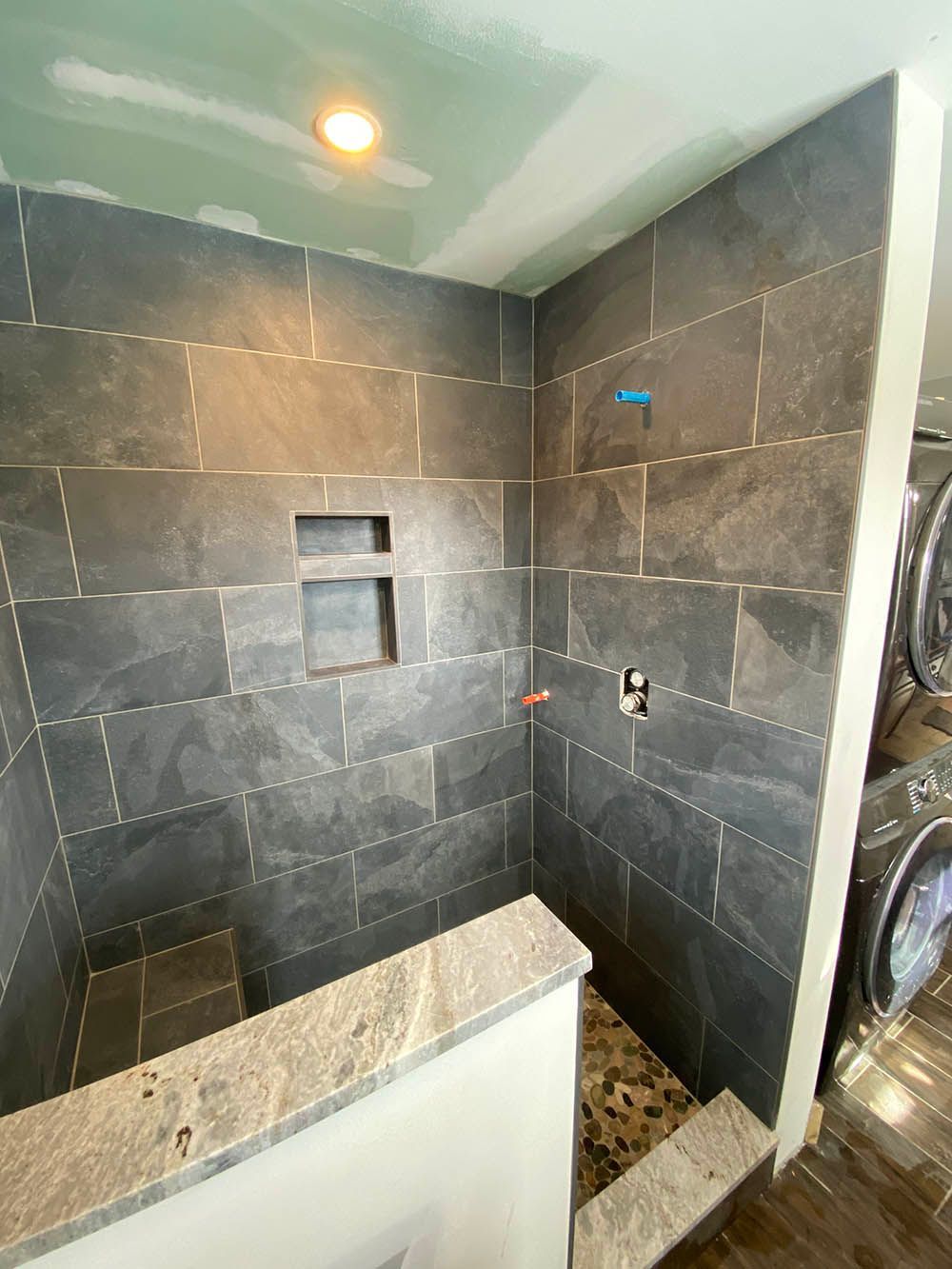 A bathroom with a walk in shower and a washer and dryer.