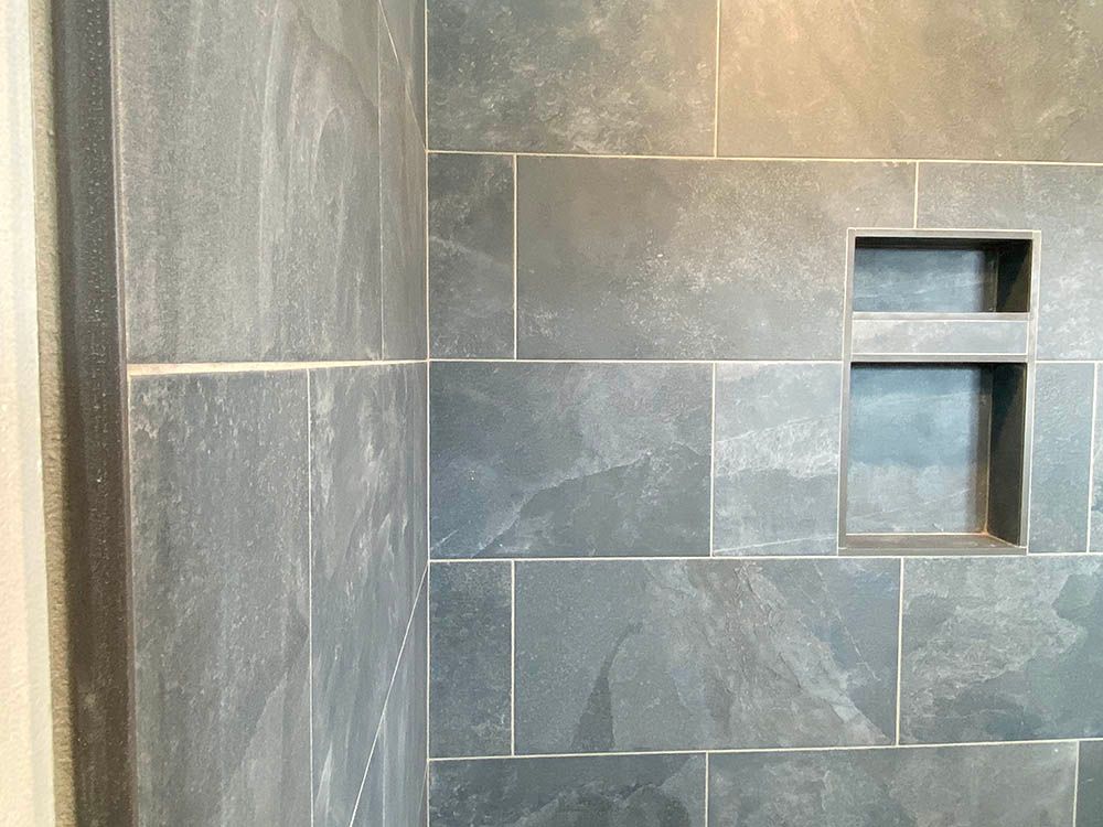 A close up of a shower wall with tiles and a shelf.