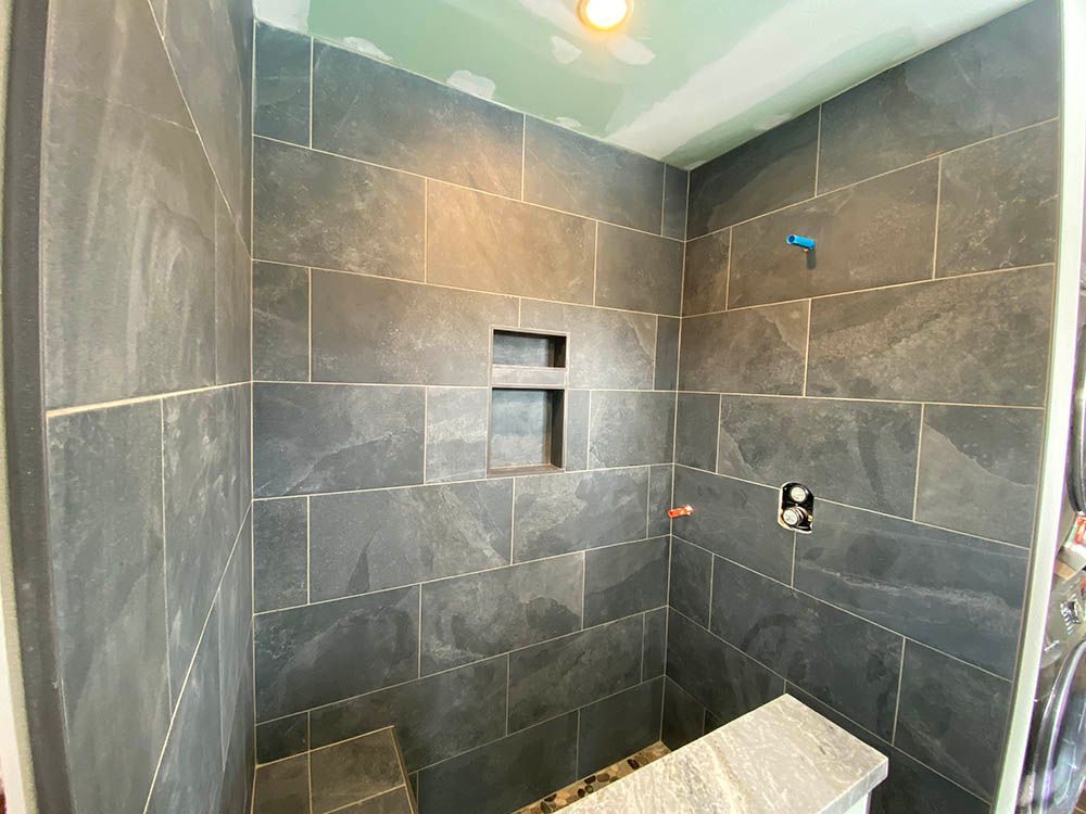A shower stall with black tiles and a bench.