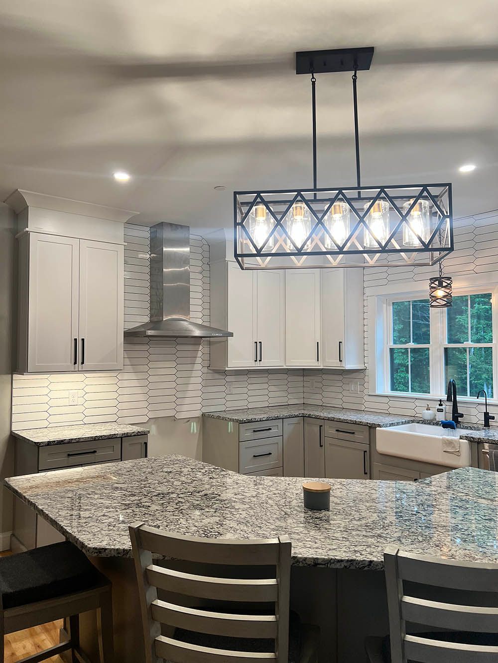 A kitchen with granite counter tops , white cabinets , a sink , and a chandelier hanging from the ceiling.