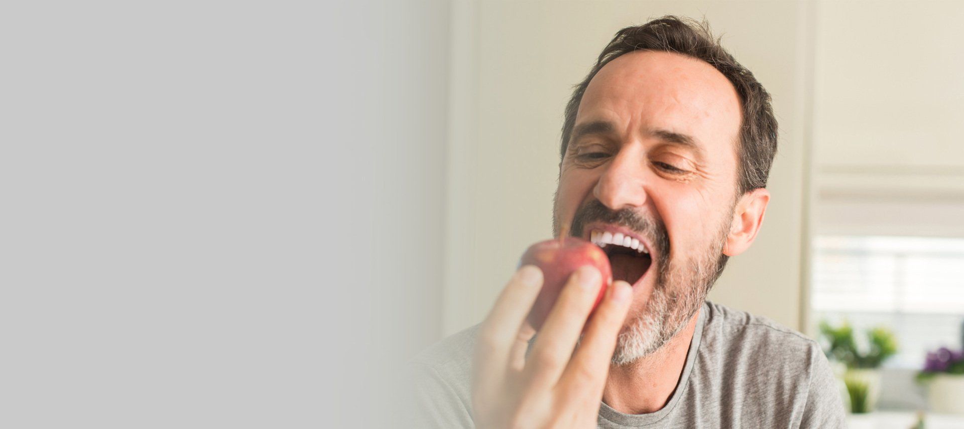 Man taking a bite of a red apple, mouth open. Indoor setting with a white background.