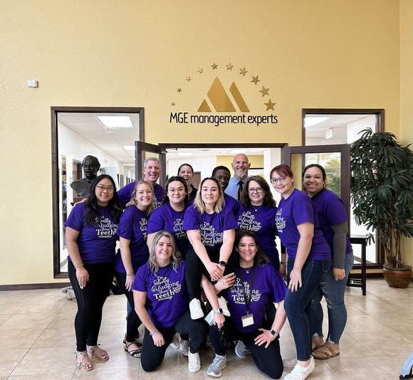 Group of people wearing purple t-shirts pose in front of a building with a logo.