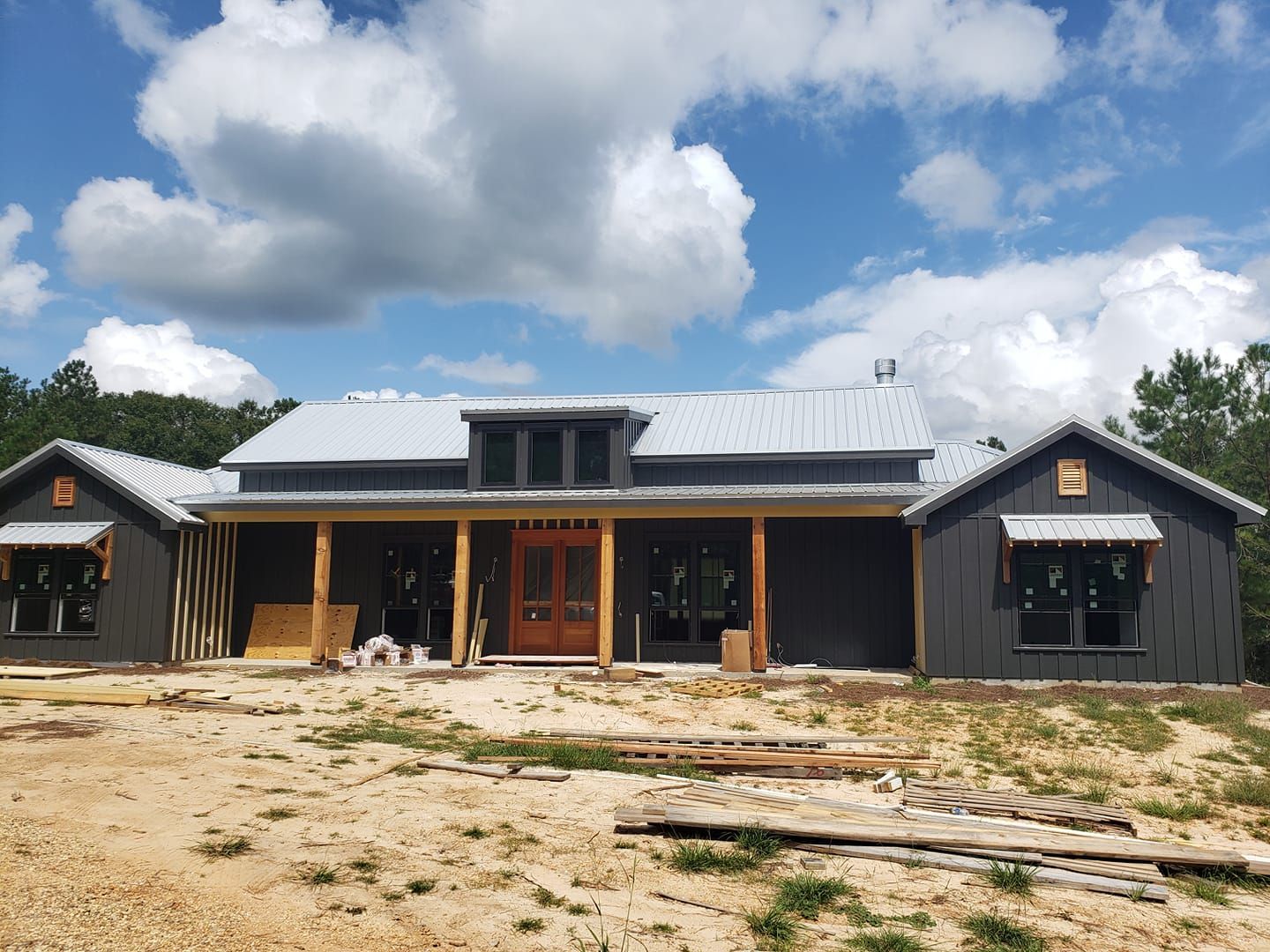 New house under construction with dark gray siding, metal roof, and wood porch. Blue sky.