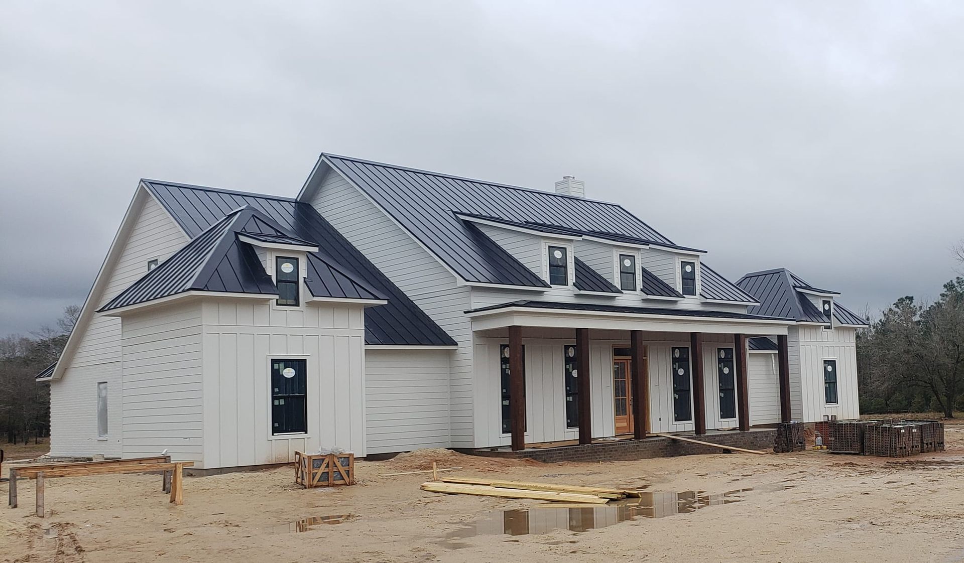 White house under construction with dark metal roof and wooden porch.