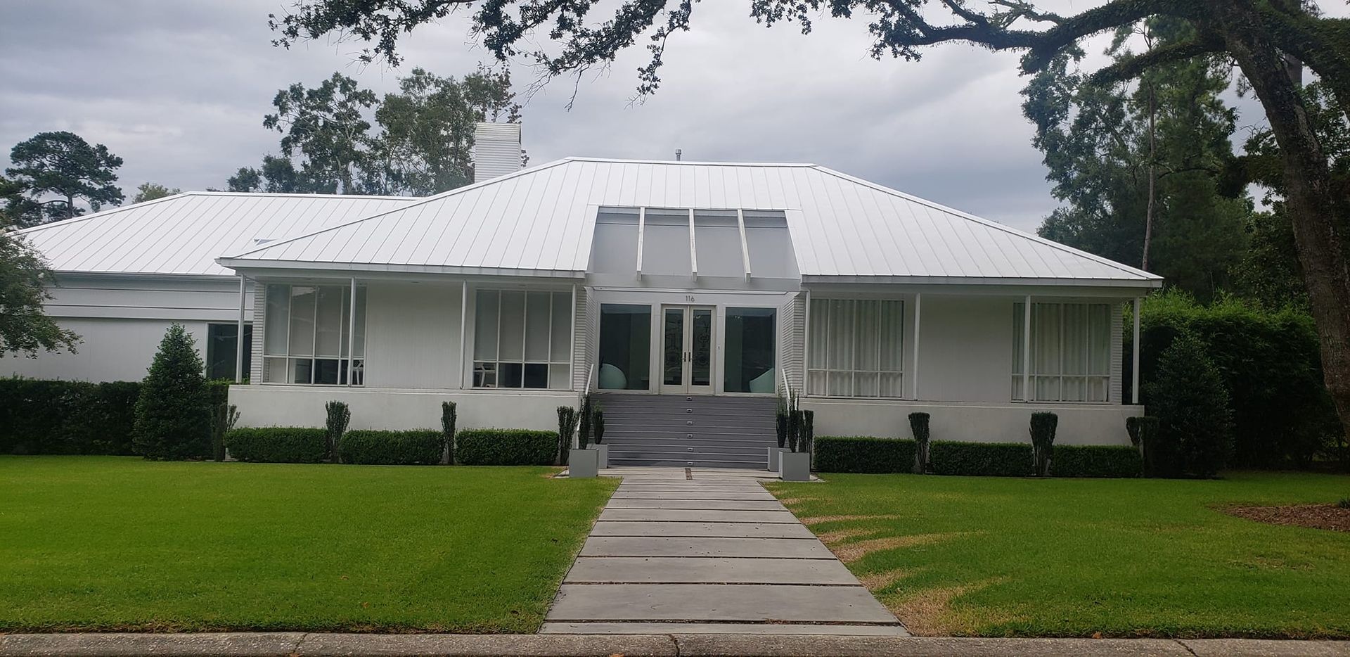 White house with white roof and lawn. Gray stone path leads to front door.