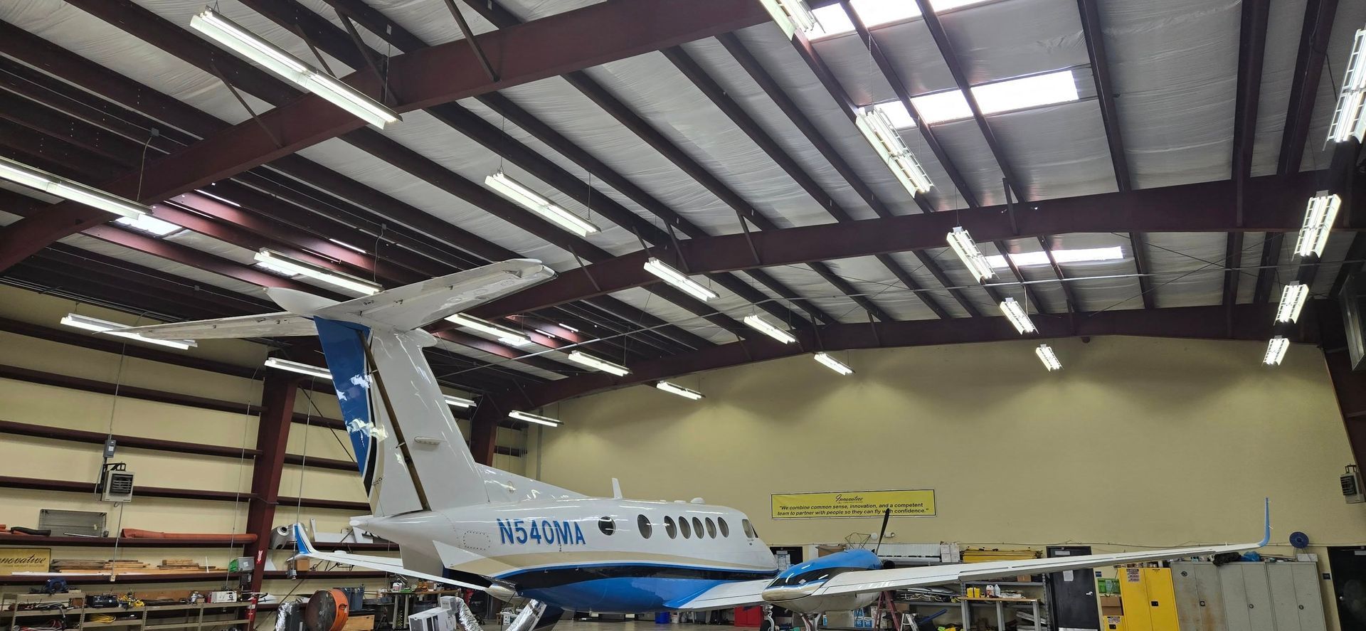 Airplane inside a hangar with a blue and white design, the roof is a brown metal structure.