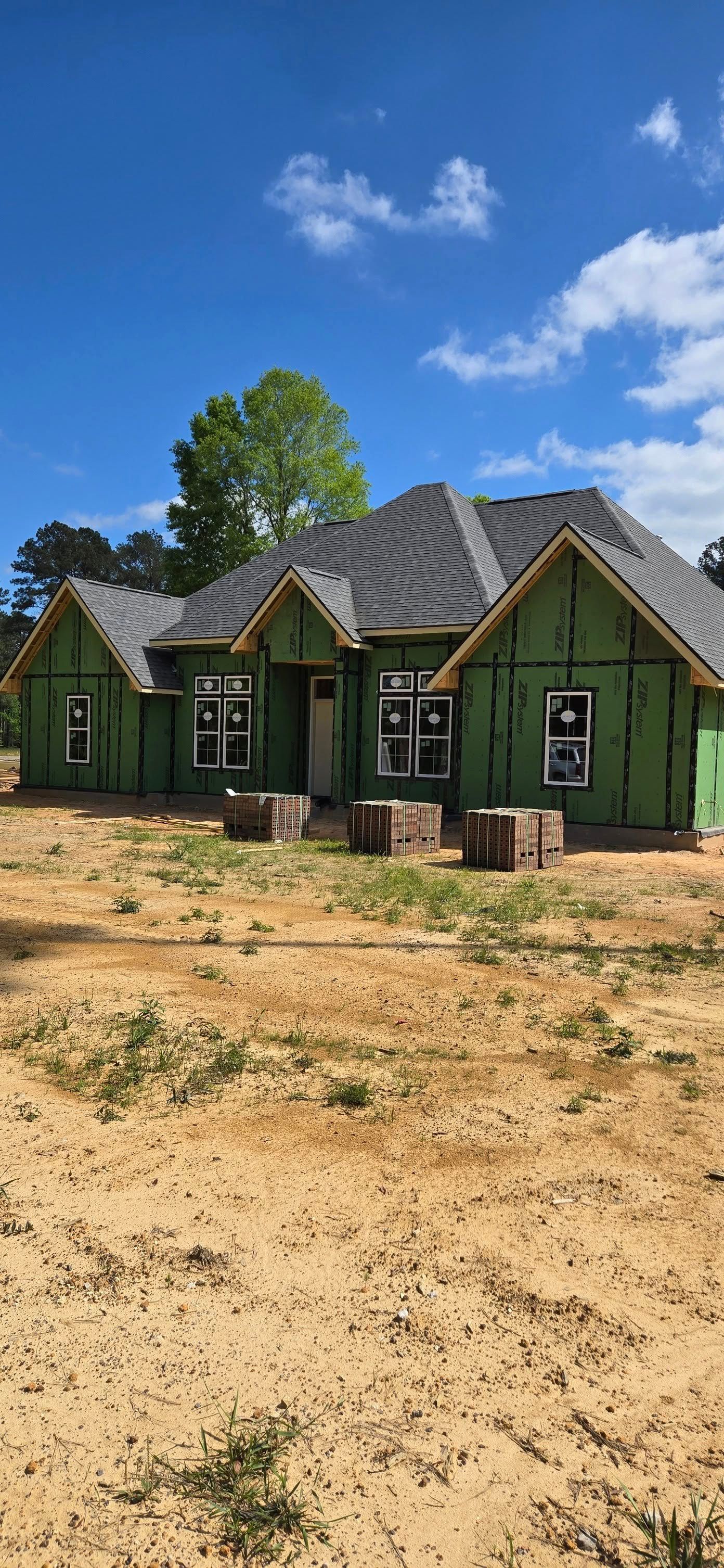 A house under construction on a sandy lot, with a blue sky background.